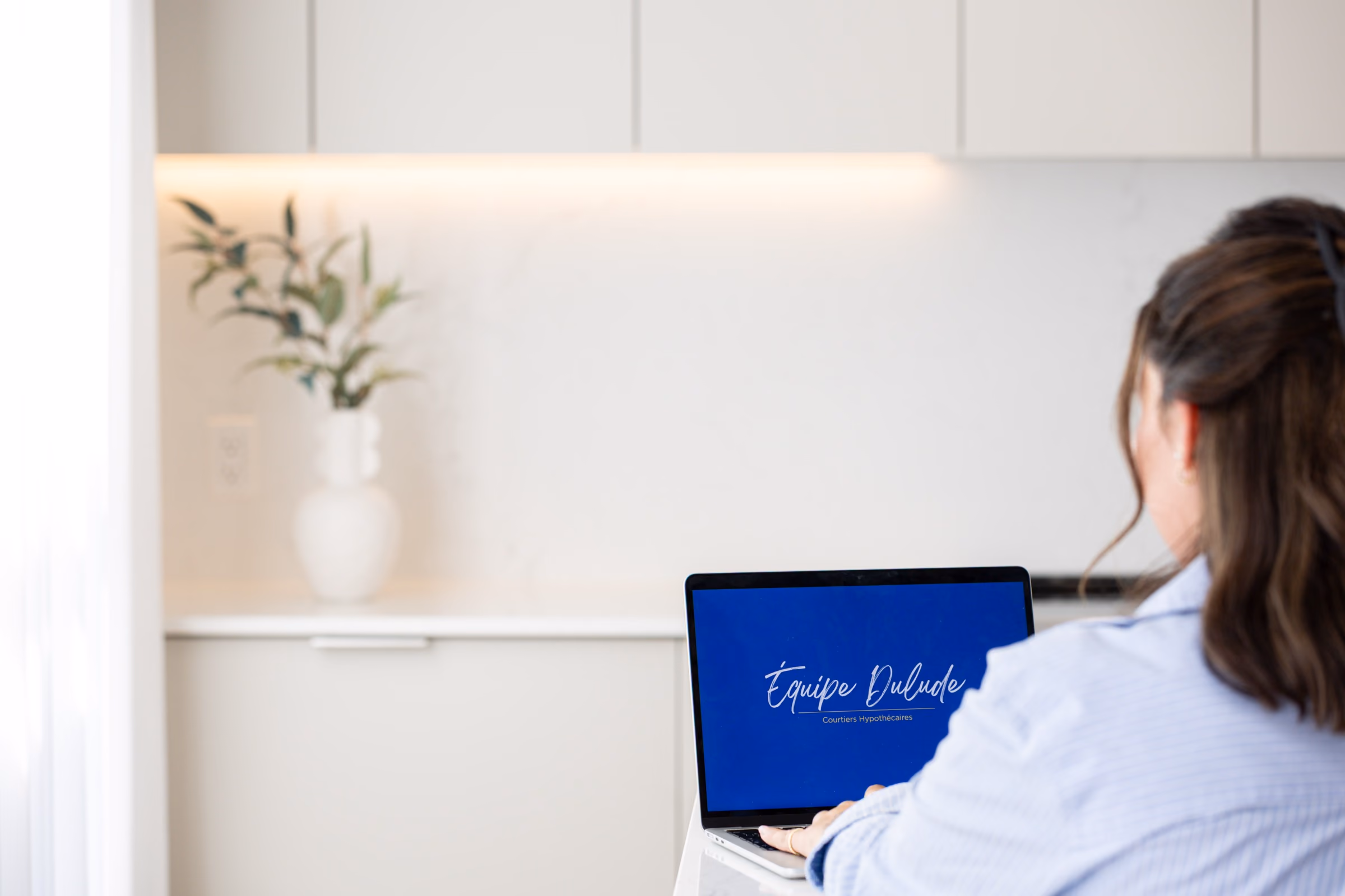 Une courtière de dos devant son ordinateur au bureau d’Équipe Dulude